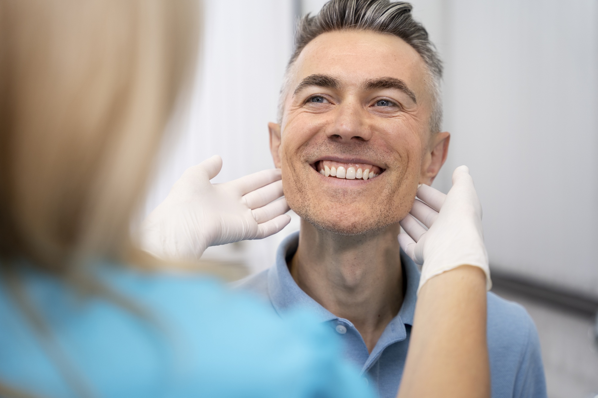 A smiling man at a dental clinic being examined by a dentist, highlighting the benefits of dental crowns for restoring a natural, healthy smile