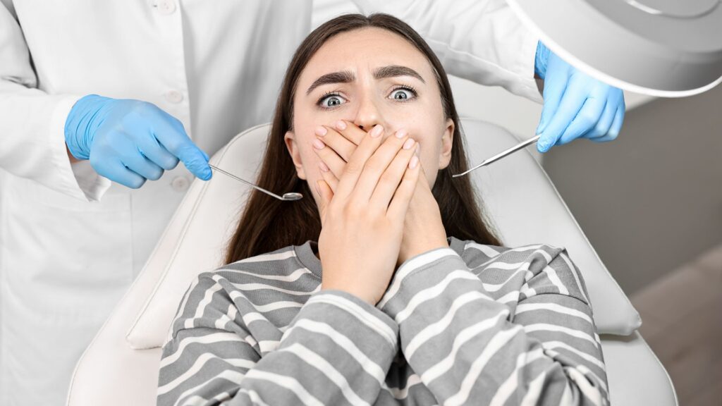 Anxious woman covering her mouth in fear at the dentist — showing signs of dental anxiety.