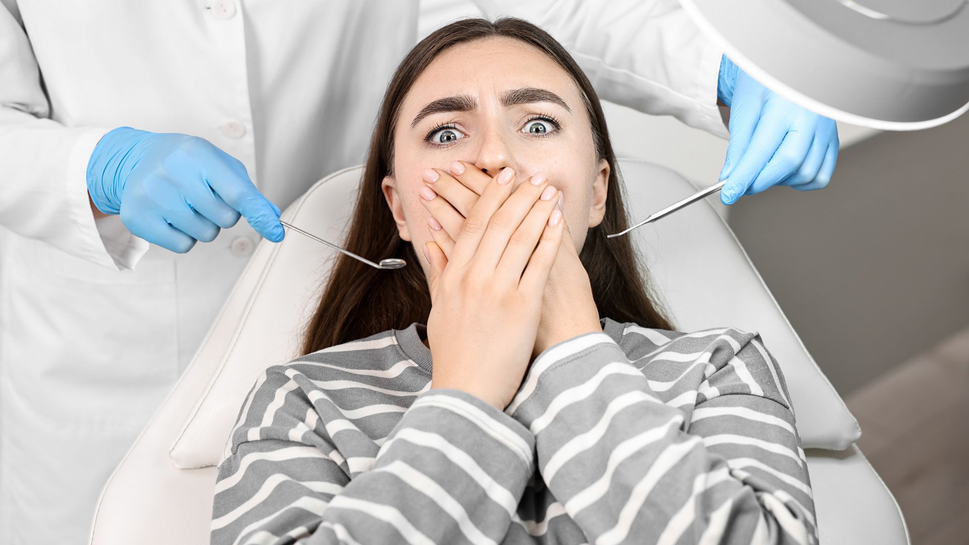 Anxious woman covering her mouth in fear at the dentist — showing signs of dental anxiety.