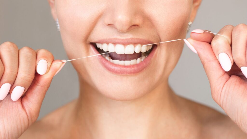 Close-up of a woman smiling while using dental floss — promoting good oral hygiene and answering how often should you floss.